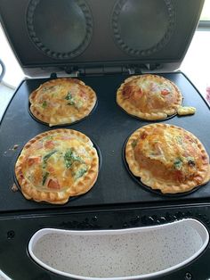 four small pizzas sitting on top of an oven