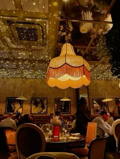 people sitting at tables in a restaurant with lights hanging from the ceiling and paintings on the walls