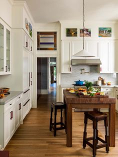 a large kitchen with white cabinets and wooden counter tops, along with two stools