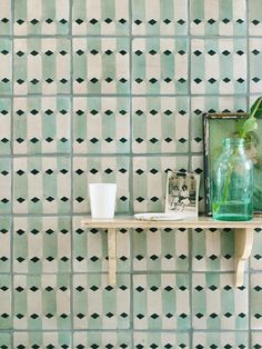 a green vase sitting on top of a wooden shelf next to a wall with black and white tiles