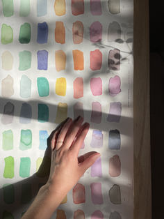 a person's hand reaching for something in front of a wall with multicolored squares on it