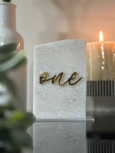 a white marble block with the word one written on it and a lit candle in the background