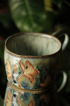 a close up of a coffee cup on a table with plants in the back ground