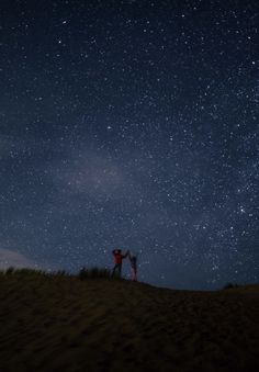 two people standing on top of a hill under the stars