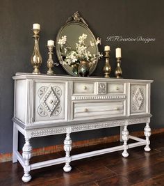 an ornate white dresser with candles and flowers on top, against a dark gray wall