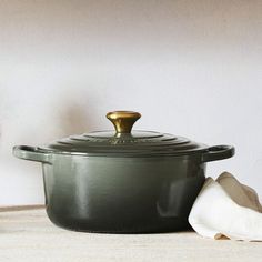 a green pot with a gold lid next to a white towel and a glass vase