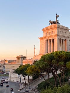 an old building with statues on top and trees in the foreground, at sunset