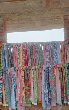 many scarves are hanging up on the wall in front of a brick building with an open window