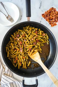 a skillet filled with green beans and bacon on top of a marble countertop