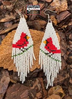 two white and red beaded earrings sitting on top of some brown rocks next to each other