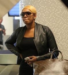 a woman in black jacket carrying a brown bag and looking at her cell phone as she walks through an airport