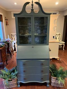 a blue china cabinet sitting on top of a hard wood floor next to potted plants