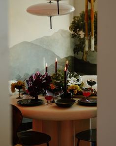 a table with candles and flowers on it in front of a mountain scene painted on the wall