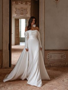 a woman in a white wedding dress standing in an ornate hallway with her hands on her hips