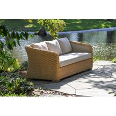 a wicker couch sitting on top of a stone walkway next to a lake and trees