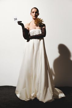 a woman in a white dress and black gloves holding a vase with flowers on it