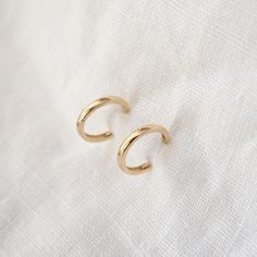 two gold hoop earrings sitting on top of a white cloth covered tablecloth, with one earring in the shape of a crescent