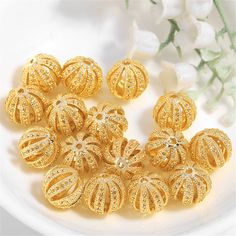 a bunch of gold colored beads sitting on top of a white plate next to flowers