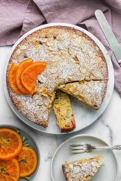 a cake with orange slices and powdered sugar on top, next to a bowl of fruit