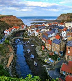 boats are parked on the water in front of some buildings and cliffs near the ocean