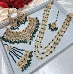 an assortment of green and gold necklaces on display in a box next to a red rose