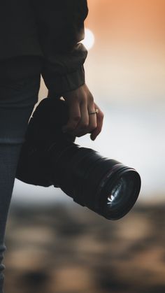 a person holding a camera with the lens pointed up to their left side, in front of a blurry background