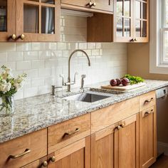 a kitchen with wooden cabinets and marble counter tops, along with white flowers in a vase on the window sill