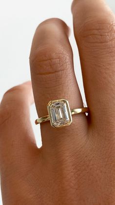 a woman's hand wearing a gold ring with an emerald stone in the center