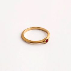 Our round ruby engagement gold ring is a dainty ring with a small ruby set within it. The ring is part of the 'Strings' ring family, a series of rings with a triangular profile and a small stone set in a variety of ways. They stack together gently, with small airy spaces between them, and can be suitable as engagement rings. The ring is made using traditional jewelry techniques to create a piece of jewelry that is classic and unique. It is elegant and comfortable to wear and will live with you h Dainty Ruby Birthstone Ring For Formal Occasions, Dainty Ruby Ring As Birthstone, Ruby Stackable Rings For Formal Occasions, Formal Gold Stackable Ruby Rings, Yellow Gold Ruby Ring With Bezel Setting For Promise, Gold Ruby Rings With Round Band, Stackable Ruby Birthstone Rings With Round Band, Ruby Stackable Rings With Birthstones, Stackable Ruby Birthstone Rings