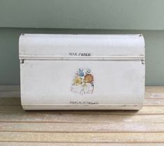 an old white box sitting on top of a wooden table next to a green wall