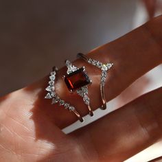 a woman's hand is holding two rings with diamonds on them and an orange stone in the middle