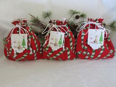 three red bags with green and white christmas tags on them sitting next to pine branches