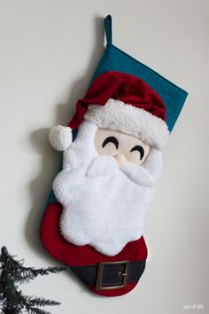 a santa claus stocking hanging on the wall next to some christmas tree branches and pine trees