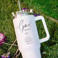 a white coffee mug with the words god is love on it sitting in some grass