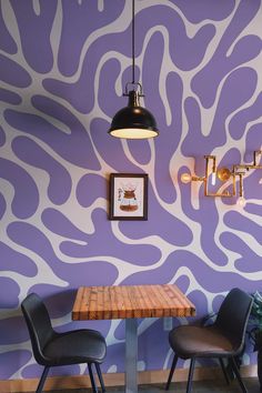 two chairs sitting at a wooden table in front of a wall painted with purple and white designs