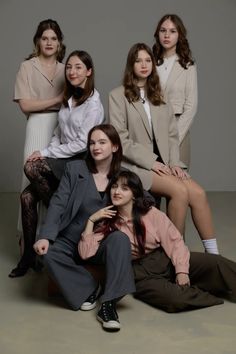 four women are posing for the camera in front of a gray background with one woman sitting on the floor