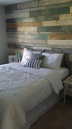 a bed with white sheets and pillows in front of a wooden headboard made from pallet boards