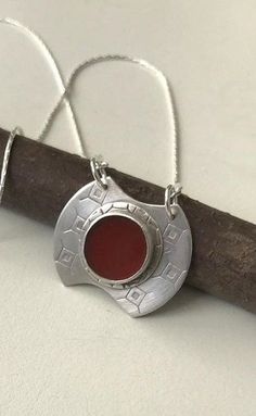 a silver necklace with a red stone in the shape of a circle on a wooden stick