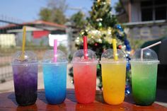 four different colored drinks sitting on top of a wooden table next to a christmas tree