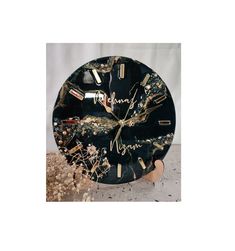 a black clock with gold numbers and writing on the face is surrounded by dried flowers