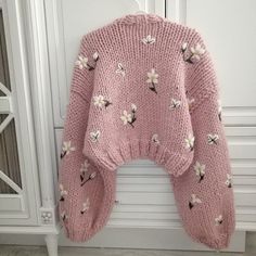 a pink sweater with white flowers on it hanging from a hook in front of a cabinet