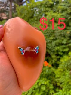 a person holding a fake butterfly earring with the price $ 15 in front of them