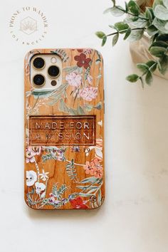 an iphone case with flowers on it next to a potted plant and a phone