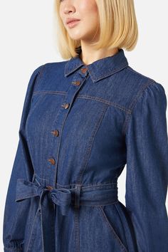 Denim long sleeve mini dress- our much loved tansy now in as a dress- classic collar- shank style button through front- detachable waist tie- length finished above the knee- panelled skirt- handy side pockets- made of lightweight cotton denim- available in dark denim Product Code: PGFX315