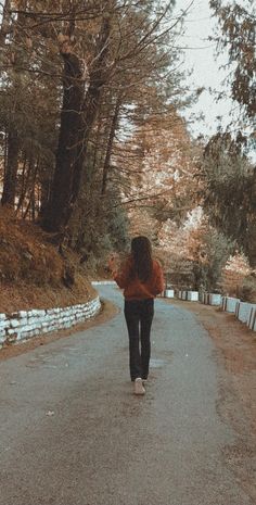 a woman walking down a road in the middle of autumn with trees lining both sides