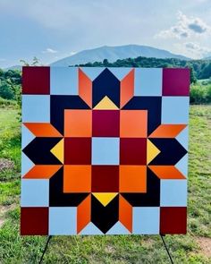 a colorful quilt sitting on top of a wooden easel in the middle of a field