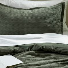 a close up of a bed with green and white sheets, pillows and a book