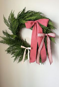 a green wreath with red and white striped ribbon hanging on the wall next to a pair of scissors