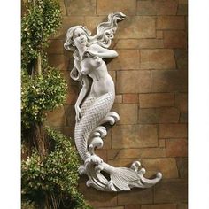 a statue of a mermaid on the side of a brick wall next to a potted plant