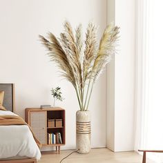 there is a plant in the vase on the floor next to a bed and nightstand